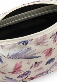 Trousse de maquillage à motifs floraux en crème, dotée d'une fermeture éclair. Intérieur doublé de tissu sombre. Texture lisse avec des bords cousus.