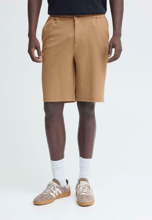 Bruine, knielange shorts gemaakt van gestructureerde stof met een elastische tailleband; gecombineerd met witte sokken tot de kuit en beige sneakers.