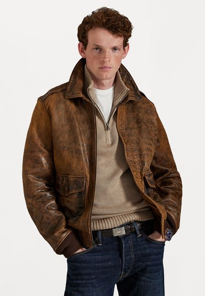 Brun læderjakke med en struktureret overflade, to forlommer og krave, lagdelt over en beige striktrøje og mørke jeans.