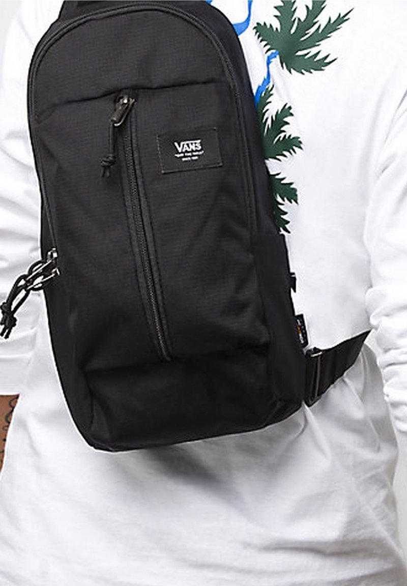 Černá zavazadlová taška s texturovaným povrchem, zipovou kapsou a logem Vans. Vybavena nastavitelným popruhem a odolným materiálem. Kompaktní design.