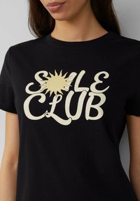 Zwarte katoenen T-shirt met witte tekst "SOLE CLUB" en een zonicoon, ronde halslijn en korte mouwen. Zacht, casual stof.