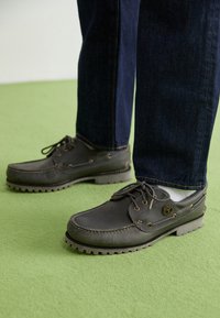 Szare skórzane buty boat z okrągłym noskiem, gumowymi podeszwami, kontrastowym przeszyciem oraz sznurowanymi detalami, w komplecie z ciemnoniebieskimi dżinsami.
