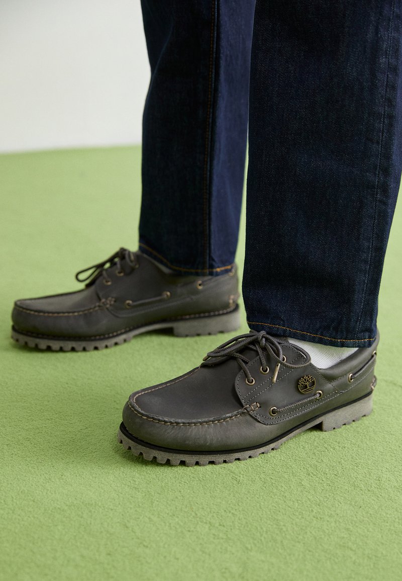 Szare skórzane buty boat z okrągłym noskiem, gumowymi podeszwami, kontrastowym przeszyciem oraz sznurowanymi detalami, w komplecie z ciemnoniebieskimi dżinsami.