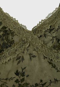 Tissu en dentelle verte avec motifs floraux et bords festonnés se croisant en forme de X au centre.
