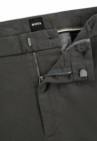 Grå byxor med en metalldragkedja och knappstängning. Har en tygetikett märkt "BOSS," tillsammans med subtila sömnadsdetaljer.