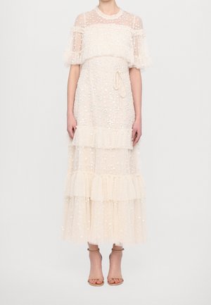 Läpinäkyvä valkoinen midi-mekko, jossa kukkakoristeita, röyhelökerroksia, lyhyet pöhötyshihat ja solmittava vyötärö, yhdistettynään alastomaan nilkkaremmi-korkokenkiin.