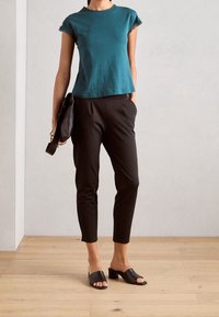 Kortärmad t-shirt i teal med spetsdetaljer, i kombination med svarta avsmalnande byxor och svarta öppna klackskor med blockklack; minimalistisk design och eleganta detaljer.