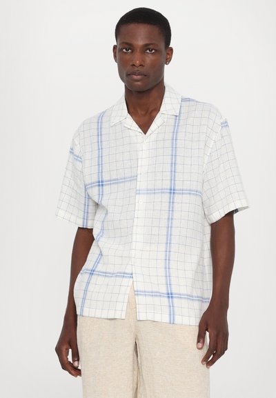 Chemise à manches courtes, boutonnée, en tissu léger présentant un motif quadrillé avec des lignes bleues et blanches. Coupe droite avec un col strié.