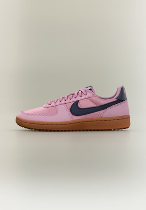 Lage roze sneaker met bruine zool en donkerblauw Nike swoosh-logo, weergegeven op een neutrale achtergrond, zijaanzicht, met veters.