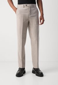 Light beige wool blend trousers with a smooth texture, flat front, and two side pockets. Paired with black shoes for contrast.