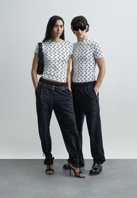 White t-shirts with black crescent pattern, paired with black joggers featuring subtle logo print. Accessories include a black bag and sunglasses.