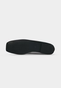 Semelle de chaussure noire avec motifs de grip texturés au talon et à la partie avant du pied, présentée sur un fond clair uni.