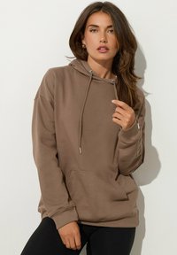 Felpa marrone con cappuccio, tasca a marsupio, cordini regolabili e polsini a coste. Tessuto morbido, vestibilità rilassata, minimi dettagli.