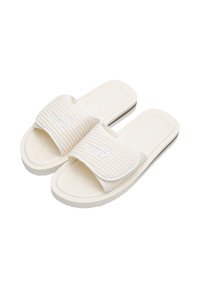 White slide sandals with a ribbed upper strap, textured footbed, and a flexible sole. Features embossed logo on the strap and sides.