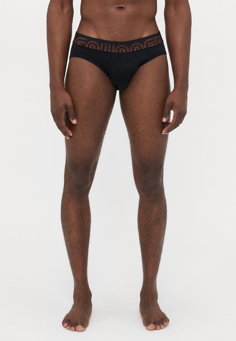Schwarze Slip-Unterwäsche im Brief-Stil mit einem gemusterten Bund in kontrastierenden Farben. Glattes Material, figurbetontes Design und minimale Bedeckung.