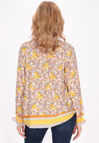 Blusa a fantasia floreale con tonalità gialle, arancioni e grigie. Maniche lunghe, polsini volant e orlo a righe. Tessuto leggero, vestibilità ampia.