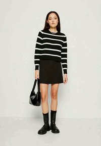 Melna un balta svītraina džemperis, pielāgots stils, apvienots ar melnu svārku. Aksesuāri ietver spīdīgu melnu rokassomu un līdz ceļiem melnas zābakus.