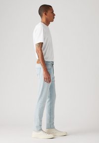 Lyseblå jeans med slim fit, hvit bomulls-t-skjorte og kremfargede sneakers, som viser et uformelt, moderne antrekk fra en sidevinkel.