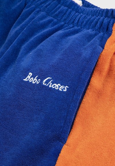 Pantaloncini in spugna blu e arancione con elastico in vita e logo "Bobo Choses" ricamato in bianco sul pannello di tessuto blu.