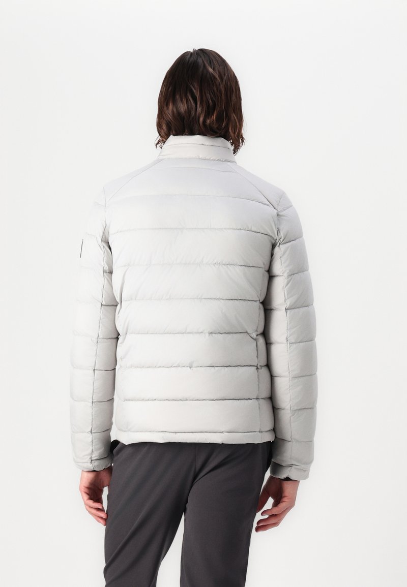 Chaqueta de plumas de color gris claro con patrón de acolchado horizontal, cuello alto y textura suave. Presenta puños elásticos y un hardware mínimo.