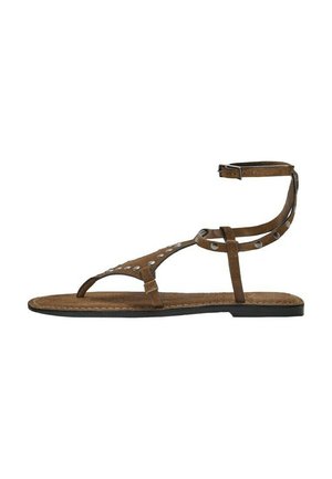 Sandalo basso in camoscio marrone con cinturino alla caviglia, cinturino per l'alluce e borchie metalliche sulle cinghie su sfondo bianco.