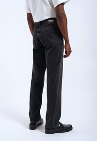 Jeans de mezclilla negra con un corte holgado, que cuentan con una etiqueta en la parte posterior, diseño de cinco bolsillos y un sutil detalle de costura a lo largo de las costuras.