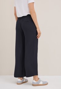 Marineblauwe wijde broek van een gestructureerde stof, met een elastische tailleband en twee achterzakken, gecombineerd met grijze sneakers met witte accenten.