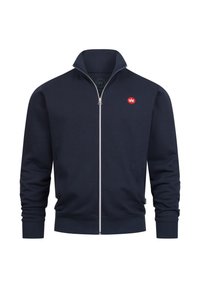 Veste zippée bleu marine avec un col montant, fabriquée en tissu doux. Dotée d'un petit logo rouge sur la poitrine gauche et de poignets ainsi qu'un ourlet côtelés.