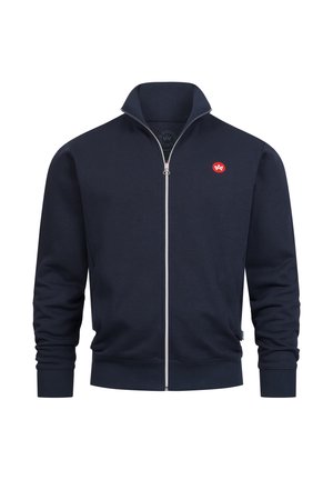 Marineblå glidelåsjakke med høy krage, laget av mykt stoff. Har en liten rød logo på venstre bryst og ribbestrikkede mansjetter og nederkant.