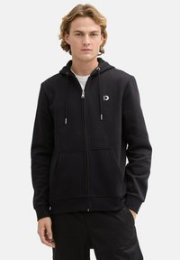 Felpa nera con zip, texture liscia, cordini regolabili, tasche frontali e un piccolo logo sul petto.