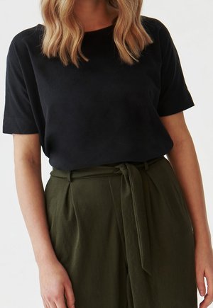 T-shirt nera a maniche corte realizzata in tessuto morbido, abbinata a pantaloni verde oliva a vita alta con dettaglio cintura. 
