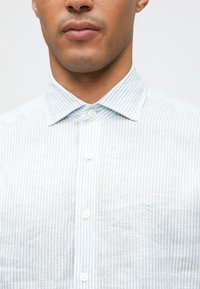 Férfi világoskék és fehér függőleges csíkos gombos ingben, hegyes gallérral és apró hímzett logóval a mellkasán.