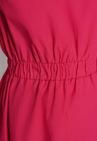 Růžové šaty s volnou siluetou, které mají nařasený elastický pas pro úzký střih a měkkou, lehkou texturu látky.