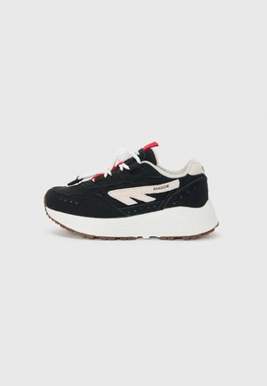 Chaussure de sport noire et crème avec une tige en daim et en mesh, design à lacets, semelle intermédiaire blanche et semelle extérieure en caoutchouc texturé. Accent rouge sur les lacets.