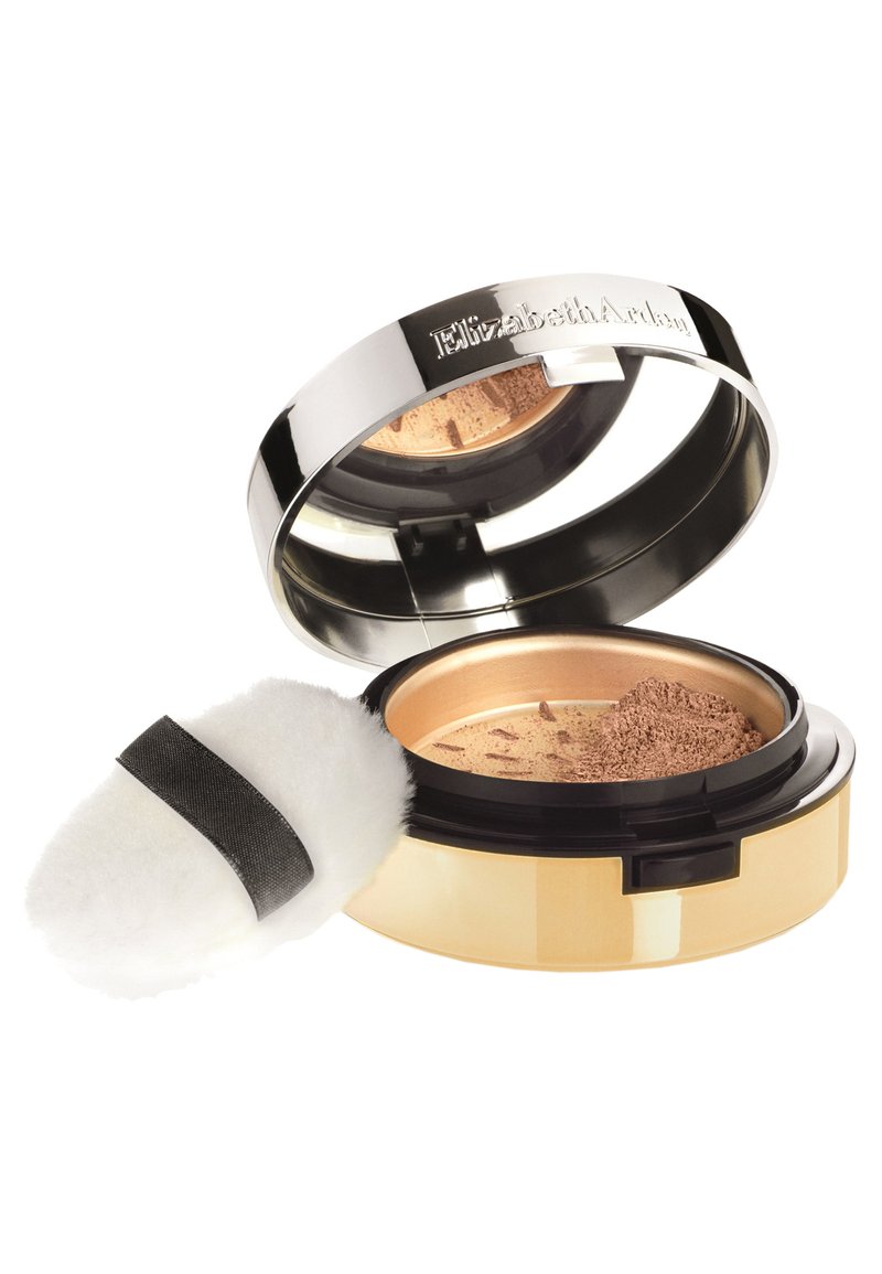 Poudre compacte dans un boîtier rond en métal avec un couvercle argenté brillant, des accents dorés et un puff applicateur doux et blanc avec une sangle noire.