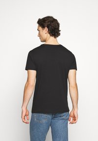 Sort bomulds t-shirt med rund halsudskæring, korte ærmer og lige kant. Båret med lyseblå jeans; viser struktureret stof og enkelt design.
