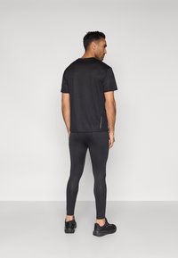 Fekete atlétikai rövid ujjú póló, fekete leggingsszel párosítva. A póló minimalista dizájnnal és enyhe oldalsó díszítésekkel rendelkezik.