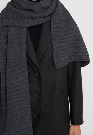 Personne portant un manteau boutonné gris foncé avec une écharpe épaisse et texturée gris charbon enroulée autour du cou et des épaules.