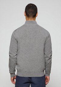Sudadera gris con cuello alzado, puños y dobladillo acanalados. Textura suave, diseño minimalista, cuenta con acentos en los hombros.
