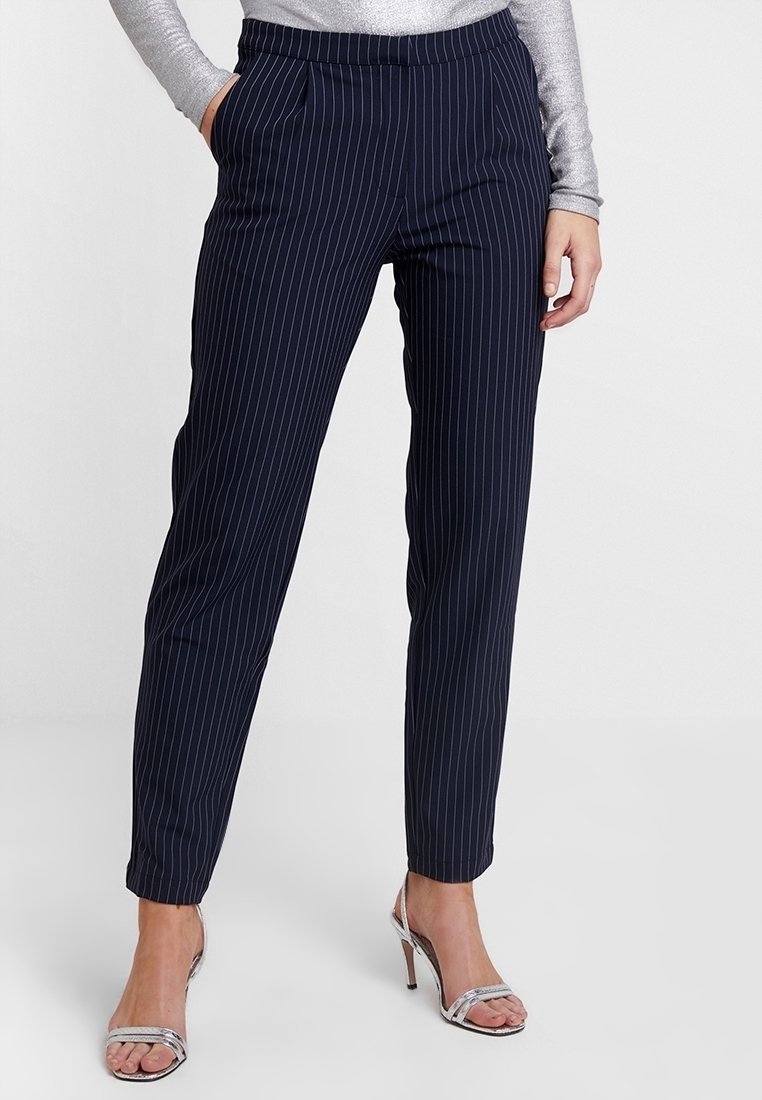 Navyblaue gestreifte Hosen mit schmalem Schnitt, ausgestattet mit Seitentaschen und einer glatten Stofftextur. Kombiniert mit silbernen Absätzen.