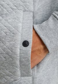 Grijze sweatshirt met gewatteerde textuur op de zak, met een zwart knoopdetail. Zacht stof met een casual ontwerp en een relaxte pasvorm.