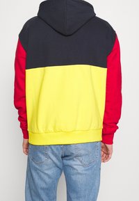 Felpa con cappuccio dal design a blocchi di colore; presenta sezioni blu navy, rosse e gialle. Materiale morbido con polsini e orlo a costine.