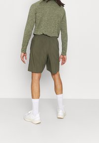 Olivgröna träningsshorts med elastisk midja, tillsammans med en långärmad grå topp. Vita strumpor och ljusa sneakers fulländar looken.