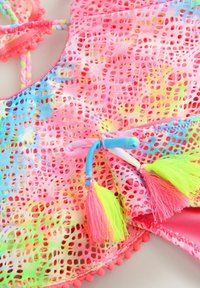 Couverture de maillot de bain colorée et légère avec un motif en dentelle, présentant des nuances de rose, bleu et jaune. Comprend des pompons et des bretelles tressées.