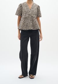 Top corto con stampa leopardata, scollatura a V e orlo svasato, abbinato a jeans ampi scuri e sandali neri bassi.