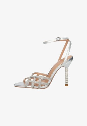 Sandalo argento con tacco alto e cinturino alla caviglia, cinturini frontali incrociati adornati con strass e tacco a stiletto testurizzato con perline.