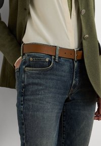Jeans i mörkblå denim med en urtvättad finish, matchade med en krämfärgad blus och ett brunt läderbälte, med silverfärgade detaljer.
