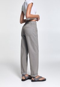 Pantalons gris amples avec une taille élastique et des ourlets à revers. Associés à un haut blanc ajusté et dessandales plates grises.