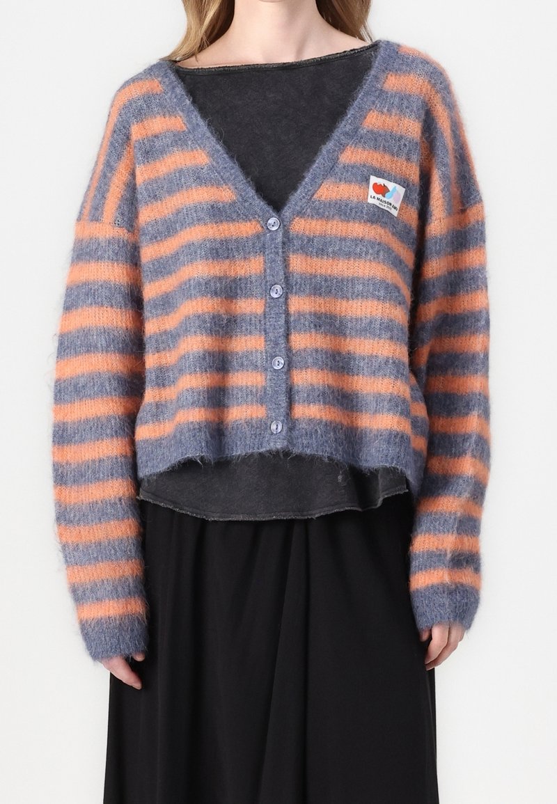 Randig kardiagan i grått och orange, tillverkad av mjukt, fluffigt material, med V-ringning, knappar fram och en patchdetalj på vänster sida.
