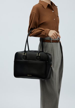 Borsa a mano in pelle nera con dettagli in oro, doppi manici e forma strutturata. Particolarità includono una tasca frontale con zip e il logo.